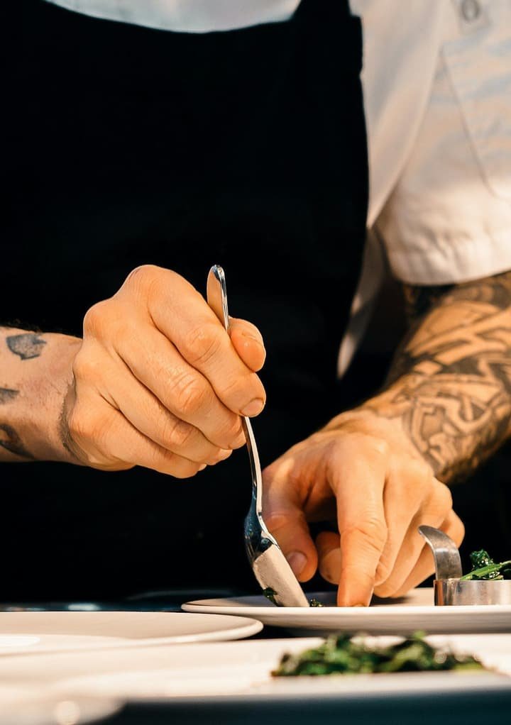 En cuisine, un cuisinier dresse une assiette à la pince