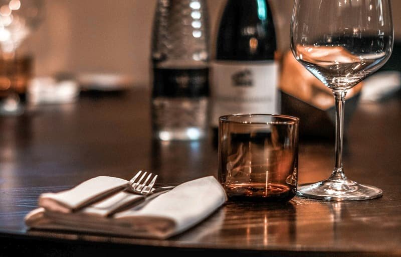 Table dressée : serviette en lin, couverts, verre à vin et gobelet ambré